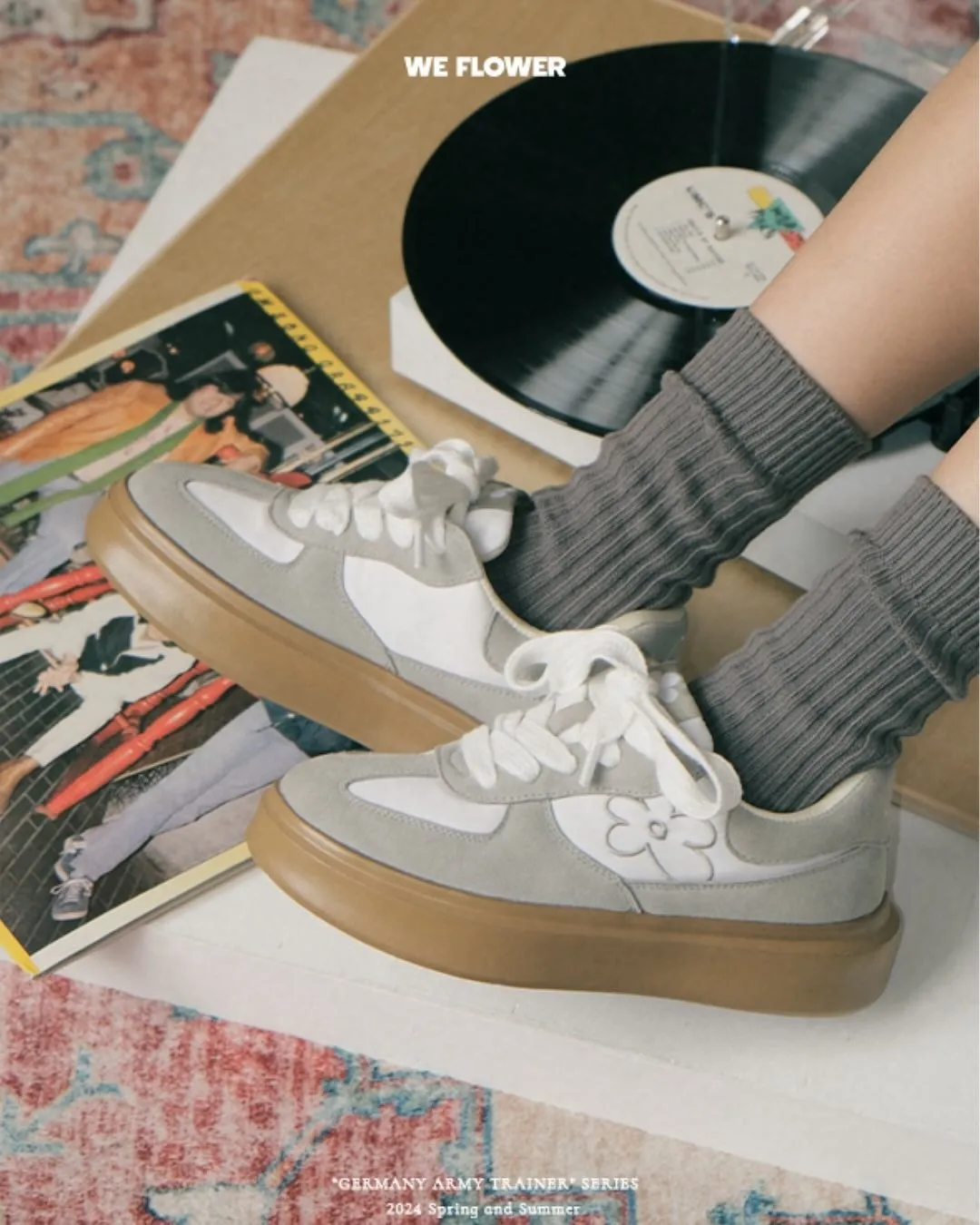 白いスニーカーを履いた足元の写真。スニーカーはグレーと白のツートンカラーで、花柄の模様が施されている。足にはグレーの靴下が履かれており、背景にはレコードと雑誌が見える。