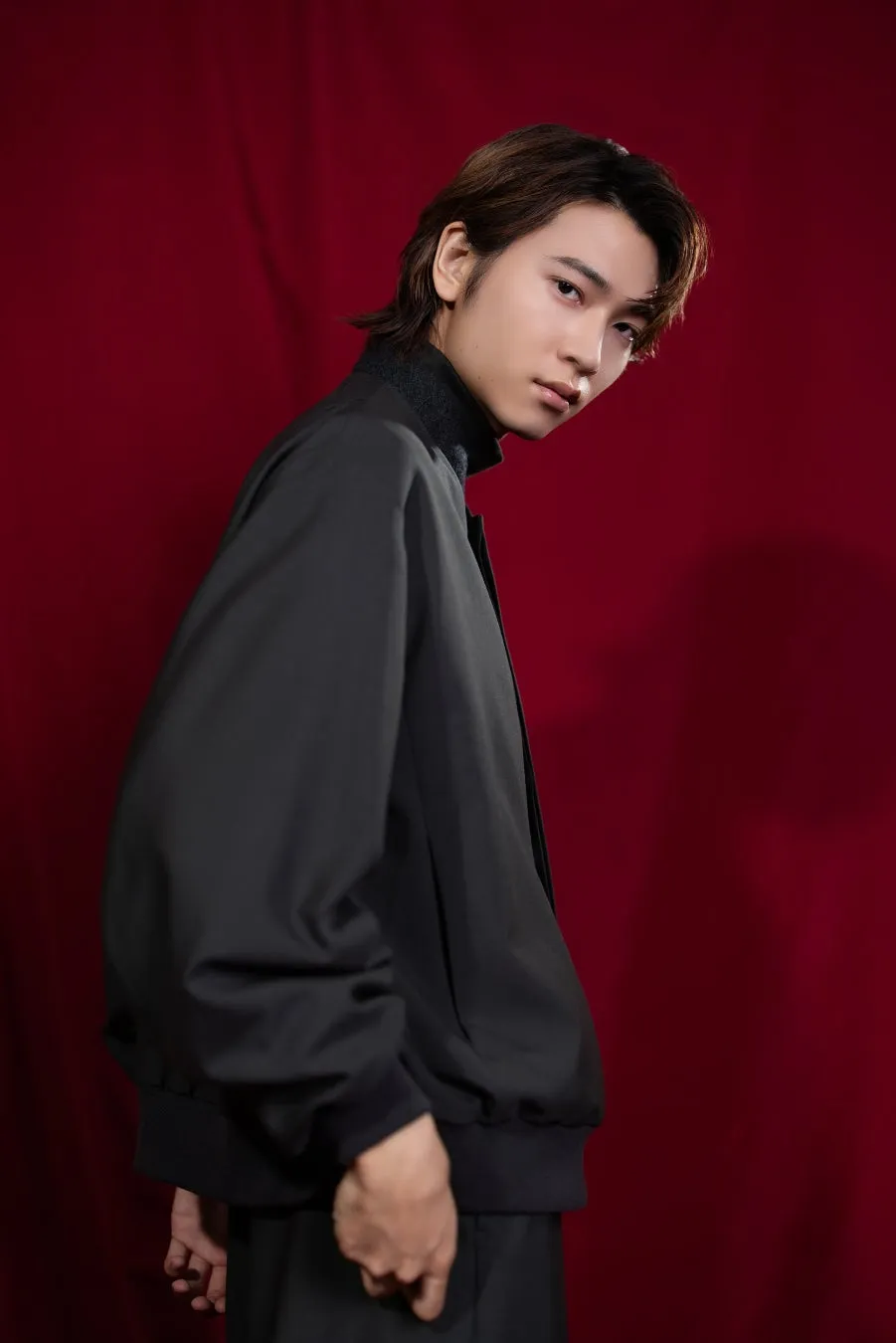 男性が黒いジャケットを着て、赤色の背景の前に立っている写真