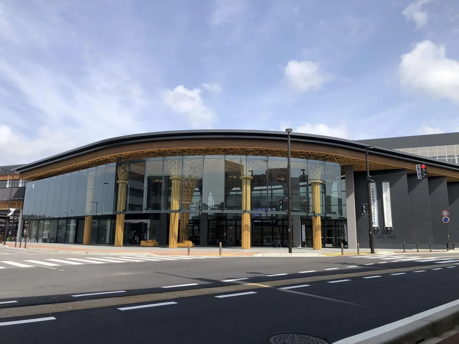 ガラス張りの近代的な建物。交差点に面しており、空には雲が見える。